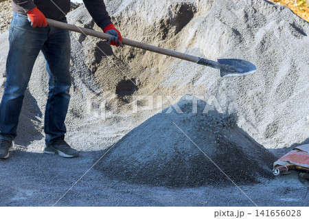 Worker is shoveling gravel at construction site is shining as materials are moved. Worker is shoveling gravel at construction site is shining as materials are moved. 141656028