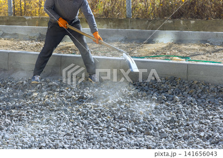 Contractor is using shovel to spread gravel on construction site dust is rising as worker moves material. Contractor is using shovel to spread gravel on construction site dust is rising as worker moves material. 141656043