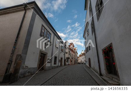 picturesque narrow historic street with traditional white buildings and cobblestone pavement under a bright blue sky with fluffy clouds in a charming European old town picturesque narrow historic street with traditional white buildings and cobblestone pavement under a bright blue sky with fluffy clouds in a charming European old town 141656335