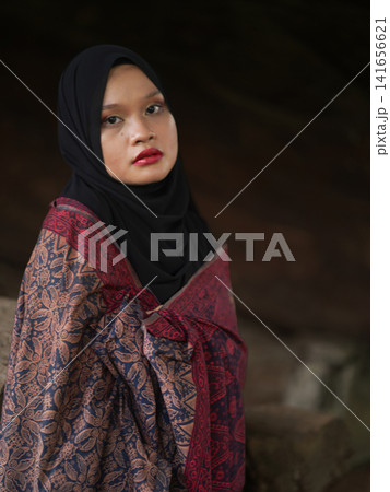 A fashionable young woman wearing a traditional black hijab and an elegant long red dress standing confidently against a weathered, vintage green door. Perfect for modest fashion, cultural, and lifest A fashionable young woman wearing a traditional black hijab and an elegant long red dress standing confidently against a weathered, vintage green door. Perfect for modest fashion, cultural, and lifest 141656621