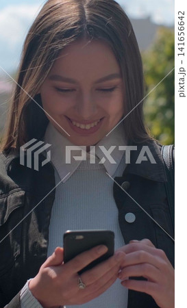 Vertical video. Young woman enjoying city streets, chatting with friends, using cellphone outdoors, beautiful sunset background. Vertical video. Young woman enjoying city streets, chatting with friends, using cellphone outdoors, beautiful sunset background. 141656642