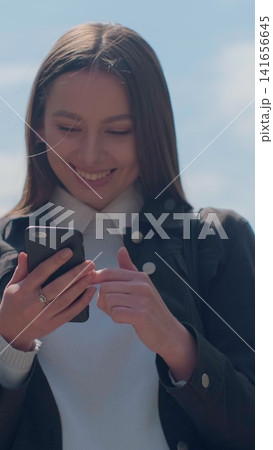 Vertical video. Young woman enjoying city streets, chatting with friends, using cellphone outdoors, beautiful sunset background. 141656645