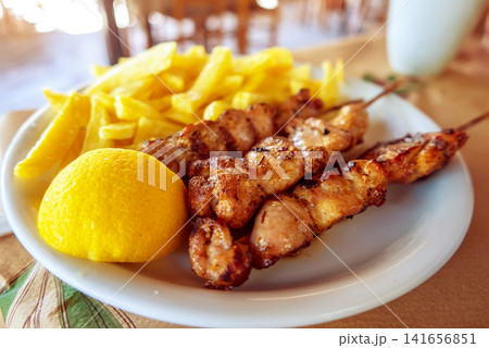 Grilled chicken skewers with fries and lemon in Greece 141656851