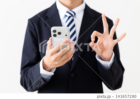 スマホを見て丸のポーズをするスーツを着た若い男性ビジネスマン 141657280