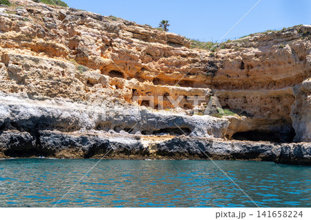 Dramatic coastal cliffs with sea caves carved by ocean waves under a clear blue sky Dramatic coastal cliffs with sea caves carved by ocean waves under a clear blue sky 141658224