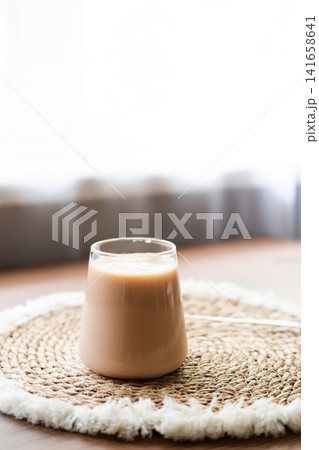 Homemade iced coffee prepared with frozen cherry juice ice cubes in a clear glass. Refreshing summer drink served on a natural woven placemat with soft daylight and minimal home interior background. 141658641