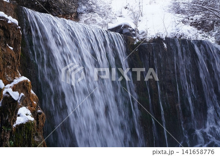 A photo of a natural landscape, where a small deep river with clear clear water breaks down like waterfall near a moss-covered steep cliff of the mountain in the winter snowy period. Beauty in nature A photo of a natural landscape, where a small deep river with clear clear water breaks down like waterfall near a moss-covered steep cliff of the mountain in the winter snowy period. Beauty in nature 141658776