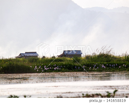 Controlled field burning near a village on Lake Inle, Myanmar, with flames, smoke, and water reflections framed by mountains at dusk Controlled field burning near a village on Lake Inle, Myanmar, with flames, smoke, and water reflections framed by mountains at dusk 141658819