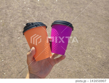 Hand holds two brightly colored coffee cups Hand holds two brightly colored coffee cups 141658907