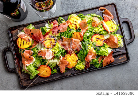 Grilled peach and prosciutto salad with green lettuce, balsamic glaze and wine on dark background Grilled peach and prosciutto salad with green lettuce, balsamic glaze and wine on dark background 141659380