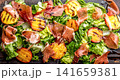 Grilled peach and prosciutto salad with green lettuce, balsamic glaze and wine on dark background 141659381