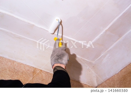 Homeowner painting ceiling with roller. Pleasant changes on budget. DIY cosmetic repair saves money, teaches new skills. Creative handling without hiring professionals Homeowner painting ceiling with roller. Pleasant changes on budget. DIY cosmetic repair saves money, teaches new skills. Creative handling without hiring professionals 141660380