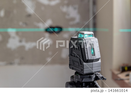 A laser level mounted on a tripod. green lines on a wall. 141661014