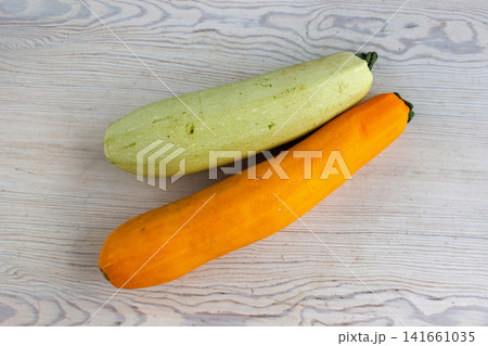Yellow and pale green zucchini on light wooden table. Minimal food composition of fresh raw vegetables and contrasting colors. 141661035