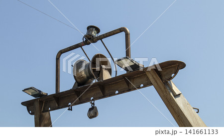 Hydraulic net drum winch and floodlights on fishing boat gantry against clear blue sky 141661133