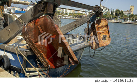 Rusty steel trawl doors hang from the stern gantry of a commercial fishing boat moored at a sea harbor Rusty steel trawl doors hang from the stern gantry of a commercial fishing boat moored at a sea harbor 141661138