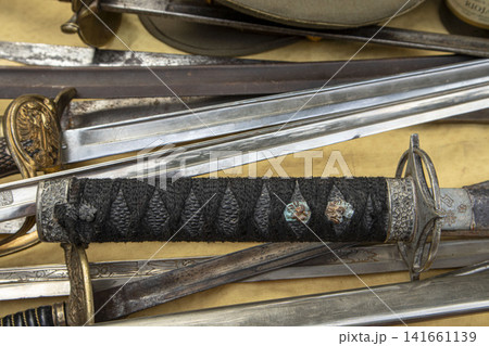Detailed view of a vintage Japanese katana hilt with cord wrapping among European cold weapons on display Detailed view of a vintage Japanese katana hilt with cord wrapping among European cold weapons on display 141661139
