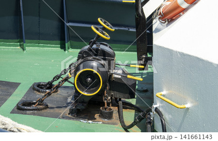 Heavy mechanical anchor windlass winch on green vessel deck showing black and yellow details with chains Heavy mechanical anchor windlass winch on green vessel deck showing black and yellow details with chains 141661143