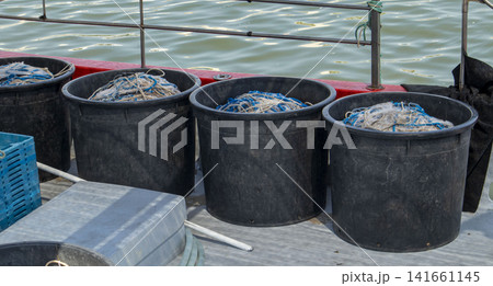Row of black containers filled with fishing nets and gear on a boat deck during a fishing trip Row of black containers filled with fishing nets and gear on a boat deck during a fishing trip 141661145