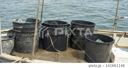 Fishing gear and heavy duty black plastic tubs stacked on the deck of a commercial fishing vessel on the water Fishing gear and heavy duty black plastic tubs stacked on the deck of a commercial fishing vessel on the water 141661146