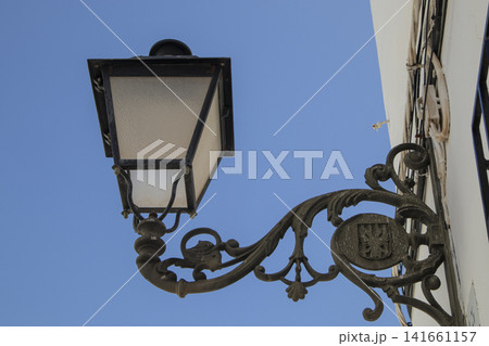 Vintage wrought iron street lamp on white building wall with blue sky Vintage wrought iron street lamp on white building wall with blue sky 141661157