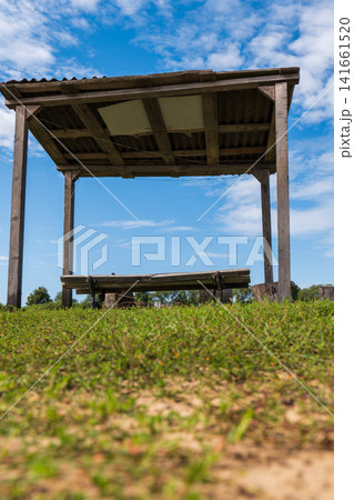 Rustic wooden shelter and bench in grassy field under bright sky Rustic wooden shelter and bench in grassy field under bright sky 141661520