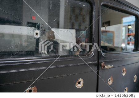 Vintage automobile door featuring bullet holes and a cracked window. The historic vehicle displays visible damage and weathered metal surfaces. Vintage automobile door featuring bullet holes and a cracked window. The historic vehicle displays visible damage and weathered metal surfaces. 141662095