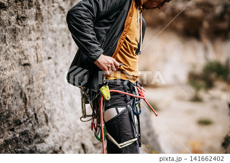 Rock Climber Attaching Ohm Device To Harness: Taped Fingers, Safety Equipment, And Rope System During Preparation At Natural Rock Wall Rock Climber Attaching Ohm Device To Harness: Taped Fingers, Safety Equipment, And Rope System During Preparation At Natural Rock Wall 141662402