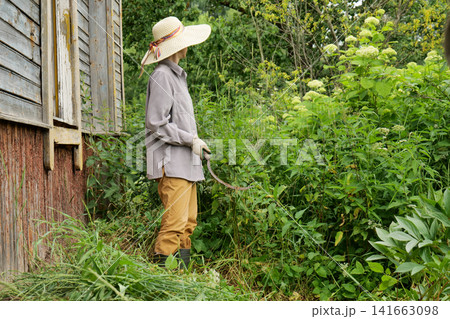 Woman in Straw Hat Weeding a Garden with a Sickle Woman in Straw Hat Weeding a Garden with a Sickle 141663098