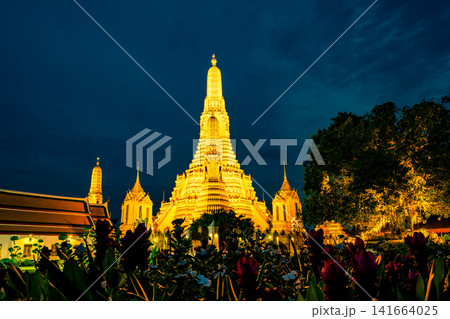 Illuminated Wat Arun Ratchawararam at blue hour in Bangkok, Thailand, glowing Buddhist pagoda, night sky. Thai architectural landmark. Historic Buddhist architecture attracting travelers worldwide. 141664025