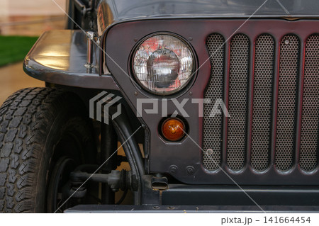 A detailed view of the front grille, headlight, and rugged construction of a vintage utility vehicle. The image highlights classic engineering and durable automotive design. A detailed view of the front grille, headlight, and rugged construction of a vintage utility vehicle. The image highlights classic engineering and durable automotive design. 141664454