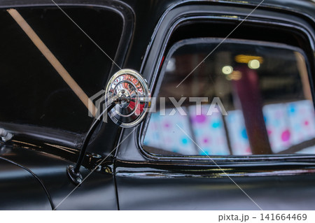 Close up of a vintage truck side mirror and window with reflections of indoor lights and colorful background. The image highlights classic automotive details, chrome elements, and glass textures. Close up of a vintage truck side mirror and window with reflections of indoor lights and colorful background. The image highlights classic automotive details, chrome elements, and glass textures. 141664469