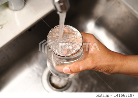 Hand holding glass under water tap at kitchen sink Hand holding glass under water tap at kitchen sink 141665187