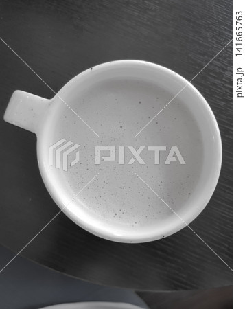 White ceramic coffee cup filled with light-colored beverage on dark wooden table surface 141665763
