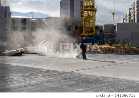 Construction worker in orange helmet cutting concrete slab with dust cloud Construction worker in orange helmet cutting concrete slab with dust cloud 141666715