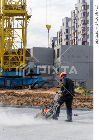 Construction worker in orange helmet cutting concrete slab with dust cloud Construction worker in orange helmet cutting concrete slab with dust cloud 141666717