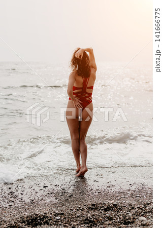 Woman beach swimsuit standing on a pebble shore facing the sea with sunlight enjoying summer vacation and relaxation Woman beach swimsuit standing on a pebble shore facing the sea with sunlight enjoying summer vacation and relaxation 141666775