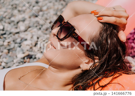 Woman beach sunglasses young lady lying on pebbly shore enjoying summer vacation sunbathing with wet hair during holiday relaxation Woman beach sunglasses young lady lying on pebbly shore enjoying summer vacation sunbathing with wet hair during holiday relaxation 141666776