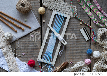 Flat lay weaving and macrame workspace with loom shuttle threads crochet hooks comb lace and craft accessories on rustic wooden table background Flat lay weaving and macrame workspace with loom shuttle threads crochet hooks comb lace and craft accessories on rustic wooden table background 141667288