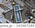Rustic weaving and macrame craft scene with loom blue threads crochet hooks comb scissors lace and handmade textile accessories on wooden table flat lay 141667289