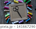 Vintage scissors on blank wooden frame surrounded by colorful sewing threads flat lay craft background with copy space for text or mockup design 141667290