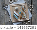 Rustic handmade craft flat lay with wooden crochet hooks decorative cords tassels wooden beads scissors and textile accessories arranged on wooden frame background top view 141667291