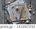 Creative handmade textile flat lay with blue decorative cord wooden crochet hooks tassels wooden beads scissors and craft accessories arranged on rustic wooden frame background 141667292
