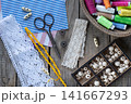 Rustic sewing and handmade craft flat lay with lace fabric colorful threads scissors buttons beads and crochet accessories on wooden background with copy space 141667293