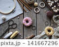 Flat lay knitting and crochet workspace with colorful donut shaped pincushions embroidery hoop scissors yarn lace and sewing accessories on rustic wooden background with copy space 141667296