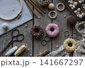 Handmade knitting and sewing accessories with colorful donut pincushions lace embroidery hoop scissors and yarn on rustic wooden background top view craft composition 141667297