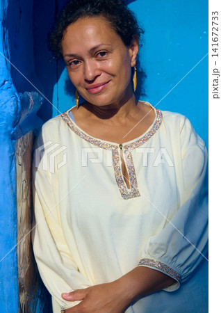 Smiling woman portrait leaning on bright blue wall in warm natural light Smiling woman portrait leaning on bright blue wall in warm natural light 141672733