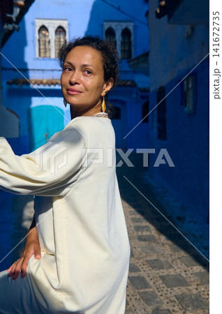 Woman in white dress posing in blue city alley of Chefchaouen, Morocco Woman in white dress posing in blue city alley of Chefchaouen, Morocco 141672735