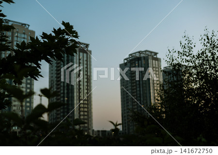 Blurred photography of a modern residential high-rise buildings at dusk with the full moon rising between skyscrapers in the evening city skyline. Blurred photography of a modern residential high-rise buildings at dusk with the full moon rising between skyscrapers in the evening city skyline. 141672750