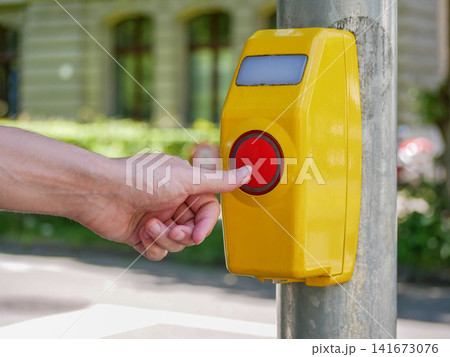Hand pressing red pedestrian crossing button on yellow signal box - urban safety, accessibility and traffic control concept. Hand pressing red pedestrian crossing button on yellow signal box - urban safety, accessibility and traffic control concept. 141673076